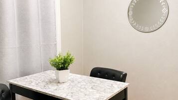 A small, modern room with a marble table, two black chairs, a potted plant, a round mirror, and a curtain.