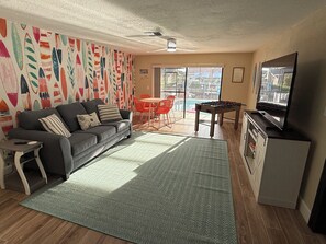A living room with a sofa, a coffee table, a TV, a foosball table, and a colorful wall.