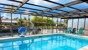 A swimming pool with a glass enclosure, surrounded by lounge chairs and a view of a residential area. - Waterfront, Gulf Access, Docks, Fishing, Games, Pool (Port Richey)