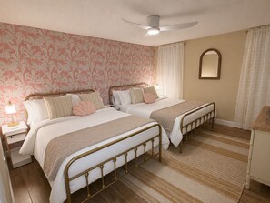 A double room with two beds, a ceiling fan, a nightstand, a mirror, and a window with curtains.