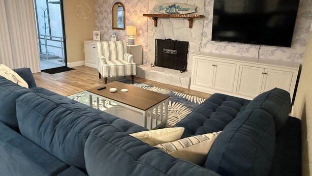 A living room with a blue sofa, a wooden coffee table, a striped armchair, a fireplace, a television, and a patterned wall. - Waterfront, Gulf Access, Docks, Fishing, Games, Pool (Port Richey)