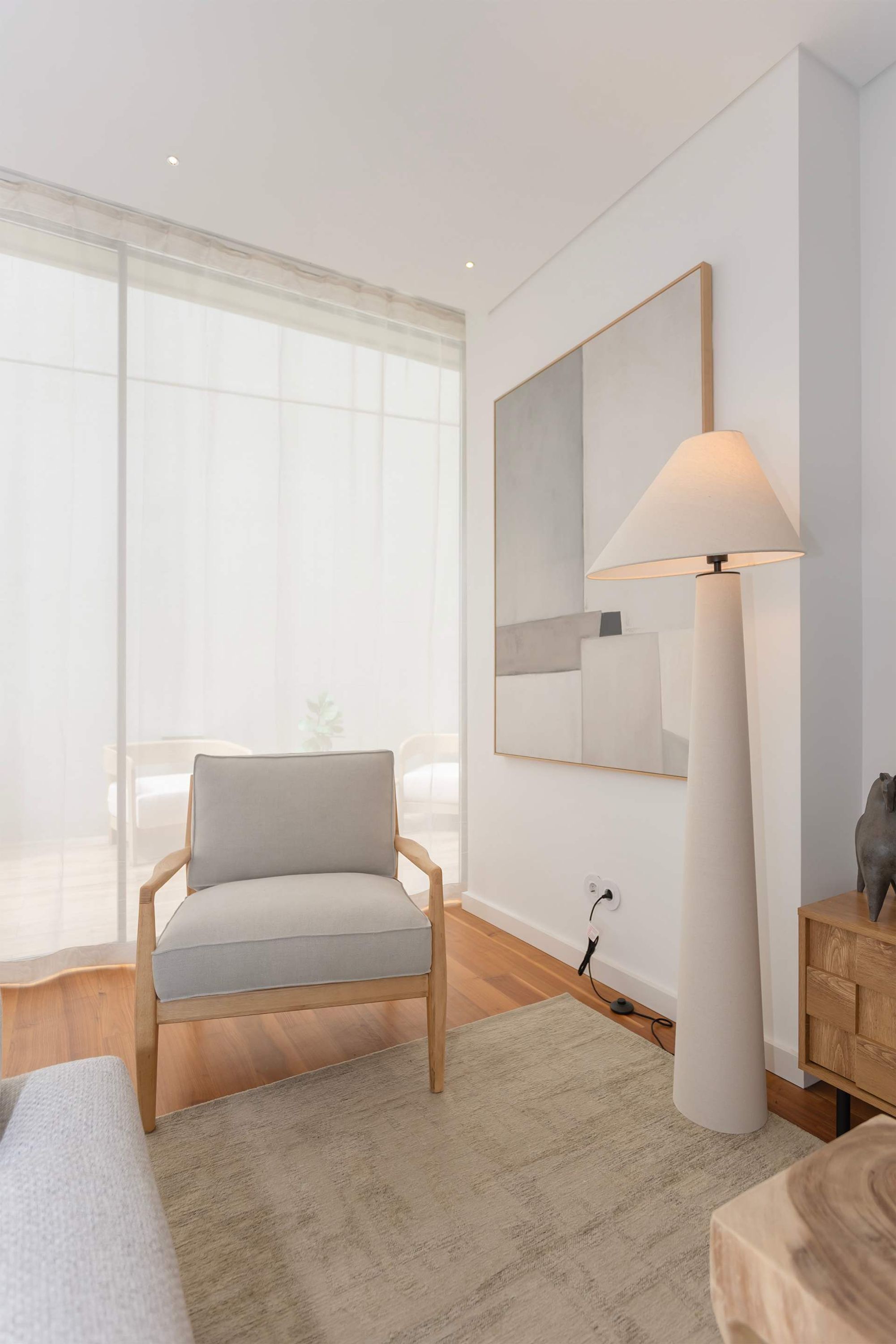 A modern room with a light-colored armchair, a large floor lamp, a mirror, and a wooden side table.