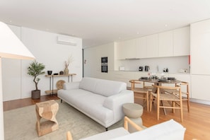 Ein modernes Wohnzimmer mit grauem Sofa, Holztisch und einem Essbereich mit rundem Tisch und Stühlen.