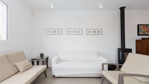 Een woonkamer met een witte bank, een fauteuil, een bijzettafeltje en een open haard.
