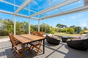 A conservatory with a wooden table and chairs, wicker seating, and a glass ceiling offering a view of greenery. - Liiiving in Gaia - Sunny Pool House (Vila Nova de Gaia)