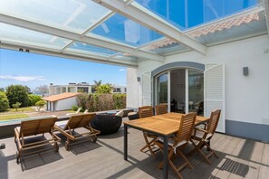 Eine überdachte Terrasse im Freien mit Tisch und Stühlen, einer Glasdecke und Blick auf die Umgebung.