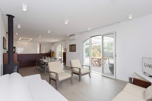 Ein modernes Wohnzimmer mit einer Couch, Sesseln, einem Essbereich und einer Küche im Hintergrund.