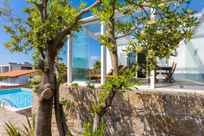 Uma casa moderna com um pátio envidraçado, piscina e muro de pedra.