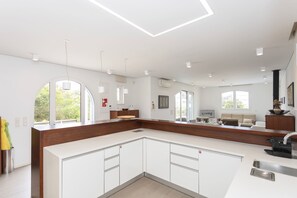 A modern kitchen with white cabinetry, a wooden countertop, and a large window. - Liiiving in Gaia - Sunny Pool House (Vila Nova de Gaia)