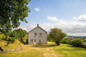 Ein eingeschossiges Haus mit Steinaußenwand, einer kleinen Veranda und einem Rasengrundstück.