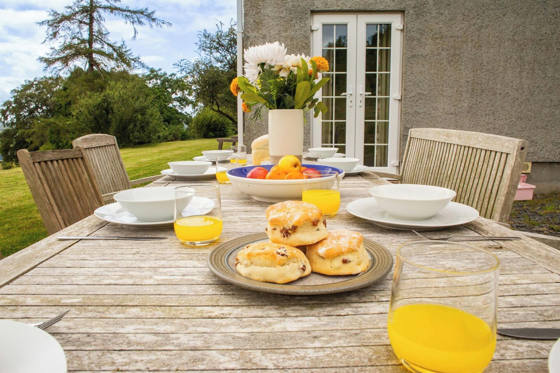A wooden table set for breakfast with bowls, glasses, and pastries.