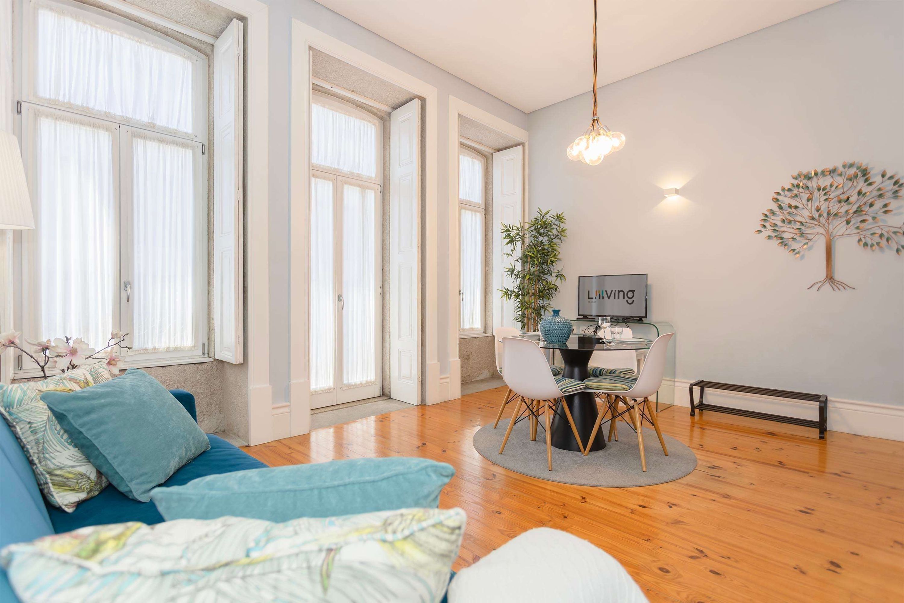 Un salon moderne avec un canapé, une table à manger et des chaises, un téléviseur et un décor mural représentant un arbre.