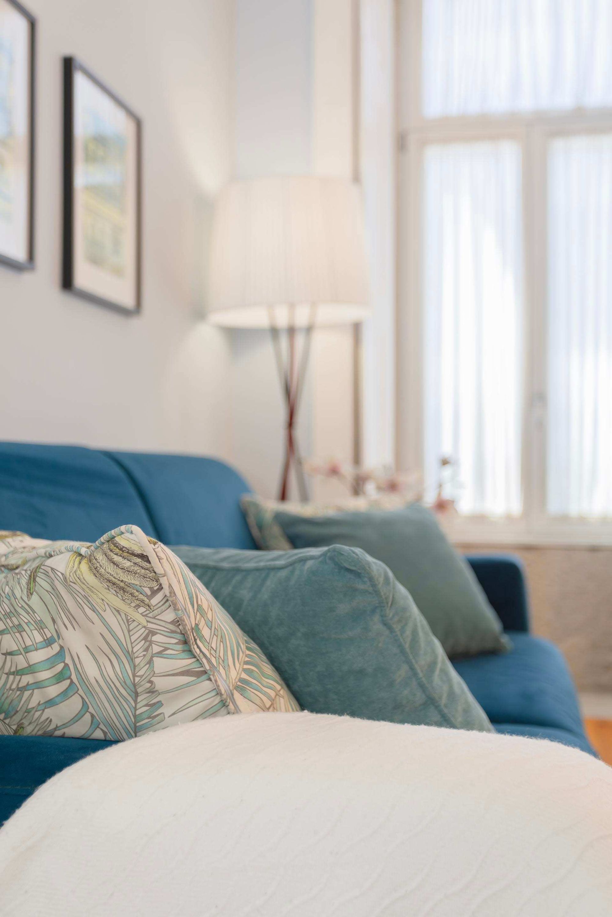 Une pièce avec un lit, un canapé bleu, une lampe et une fenêtre avec des rideaux.