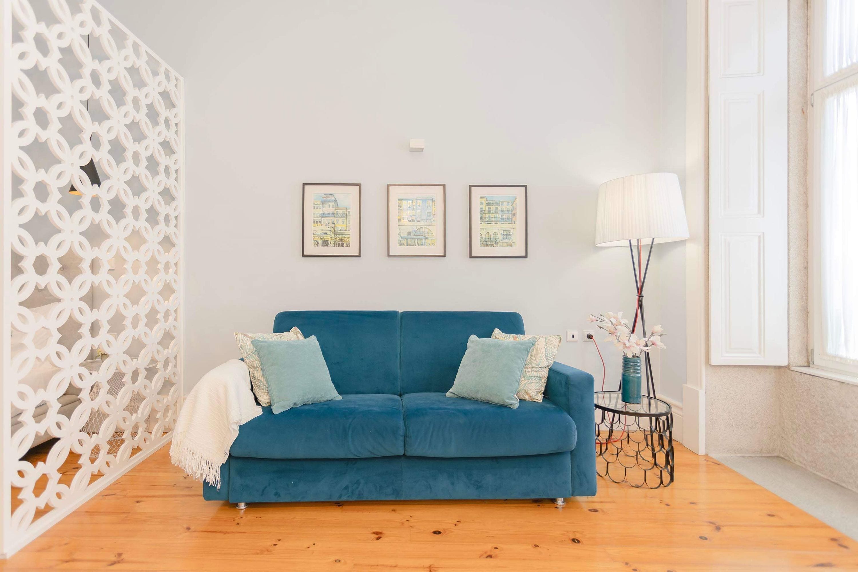 A room with a blue sofa, three framed artworks on the wall, a floor lamp, and a decorative white partition.