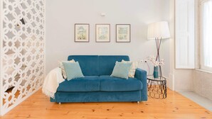 A room with a blue sofa, three framed artworks on the wall, a floor lamp, and a decorative white partition. - Liiiving in Porto - Blue Stylish Studio (Porto)