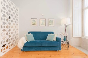 Ein Zimmer mit einem blauen Sofa, drei gerahmten Kunstwerken an der Wand, einer Stehlampe und einem dekorativen weißen Raumteiler.