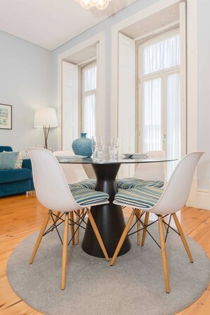 A dining area with a round glass table, two chairs with striped cushions, a blue vase, and a lamp on a blue sofa. - Liiiving in Porto - Blue Stylish Studio (Porto)