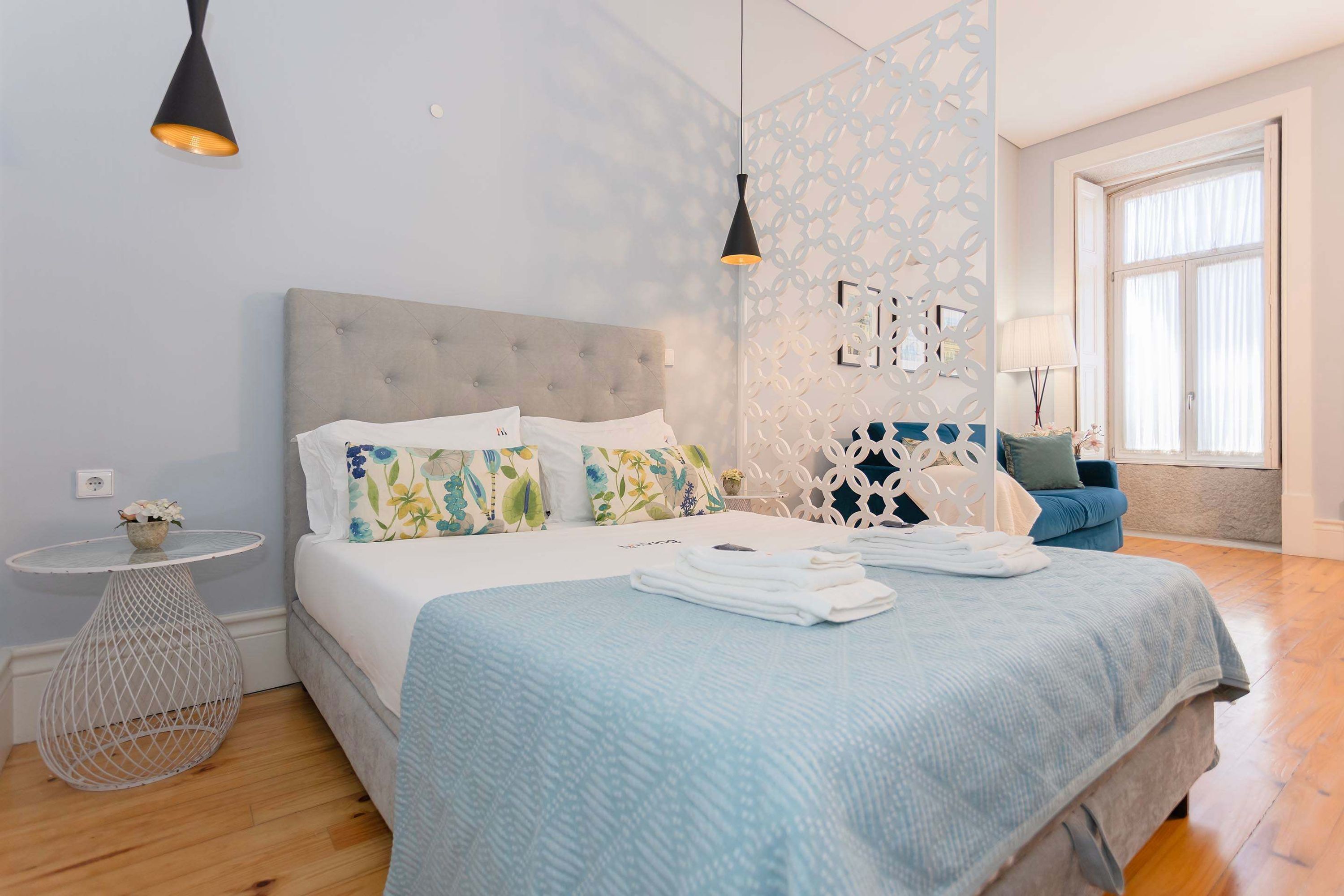 A bedroom with a bed, bedside tables, a decorative wall, and a window.