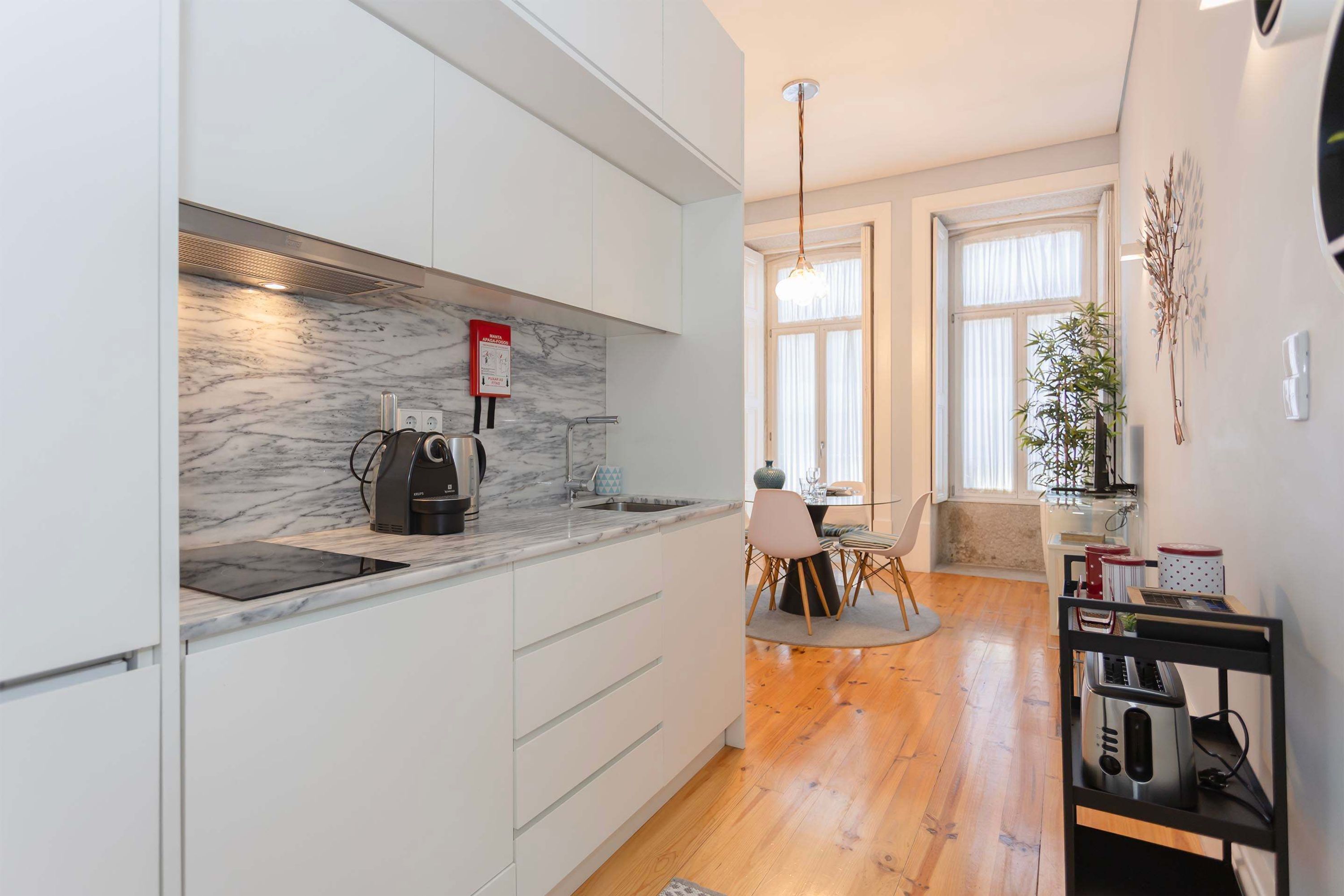 A modern kitchen with white cabinets, a marble backsplash, and a dining area with a table and chairs.
