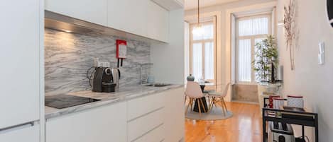 Una cocina moderna con armarios blancos, salpicadero de mármol y una zona de comedor con mesa y sillas.