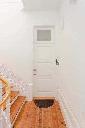 A white door with a frosted glass panel, a doormat, and a wooden staircase with white balusters. - Liiiving in Porto - Blue Stylish Studio (Porto)