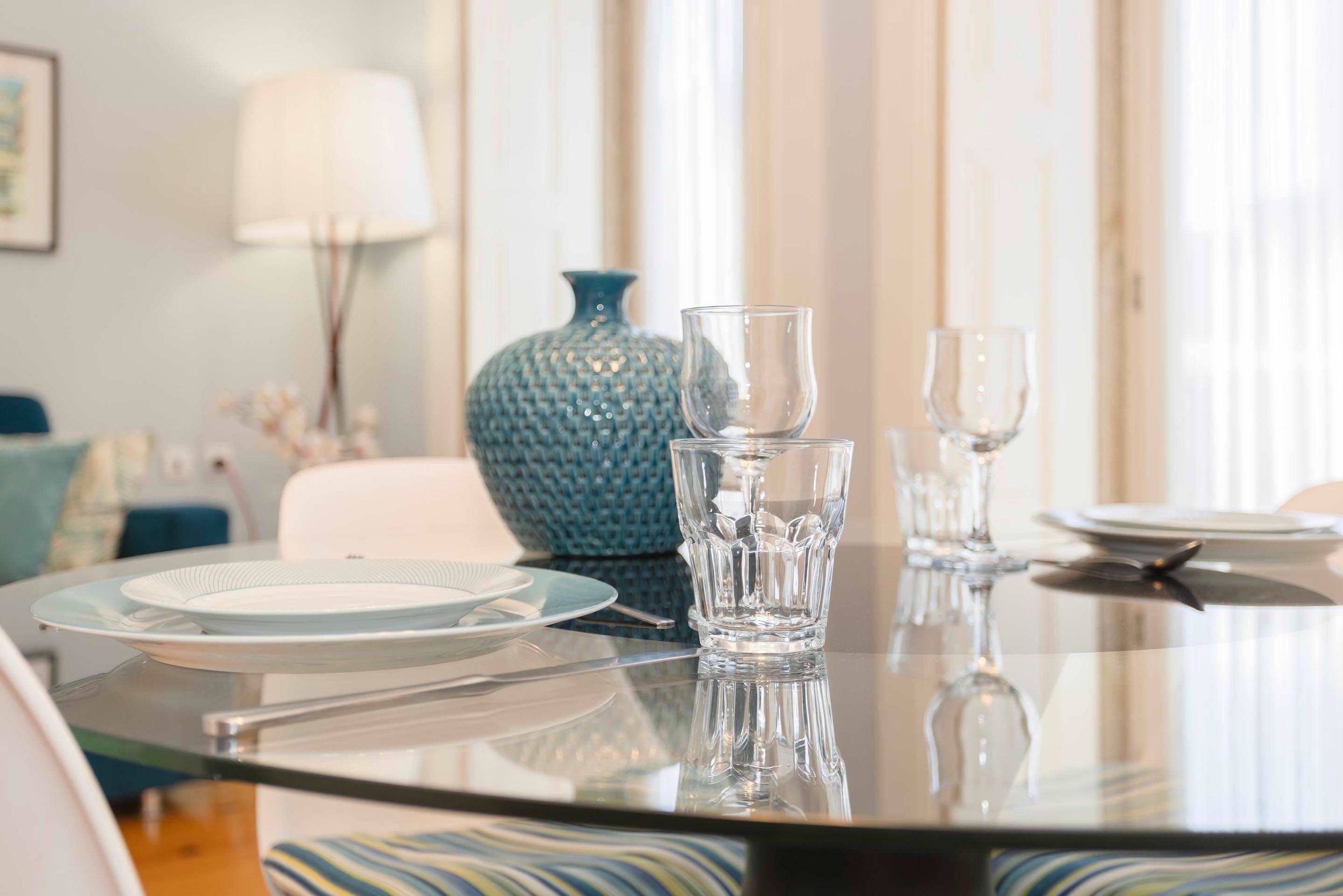 Una mesa de comedor con platos, vasos y cubiertos, en una habitación con una lámpara y un florero.