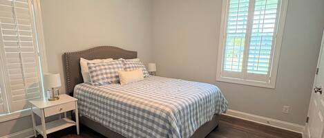 A bedroom with a bed, nightstand, ceiling fan, and a window with blinds.