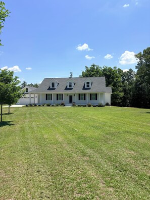 A two-story house with a front porch, a lawn, and trees in the background. - Secluded Harris Lake retreat. Nature, privacy, and Lake access to a private cove (New Hill)