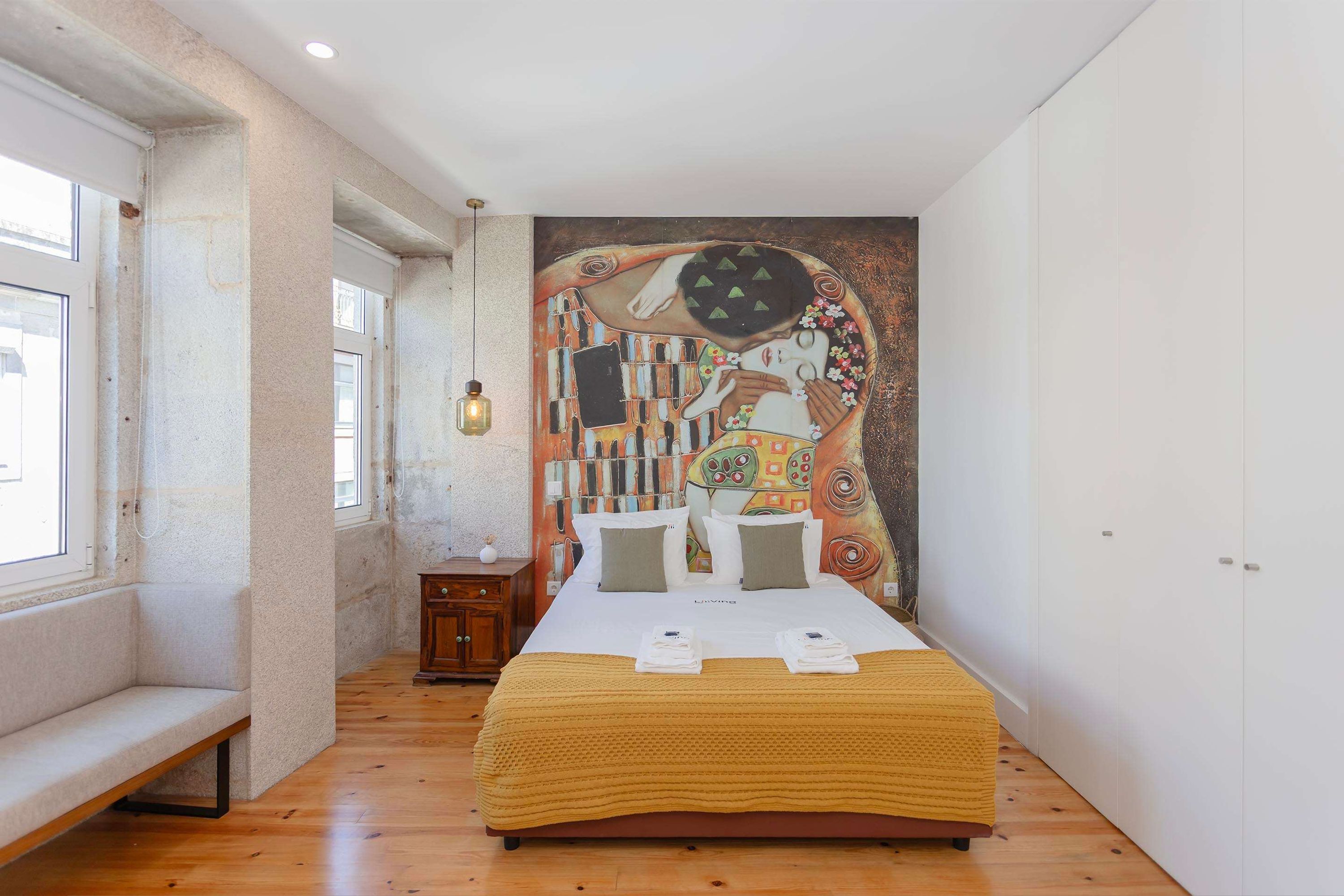 Un dormitorio con cama, una banca, una mesita y un mural en la pared.