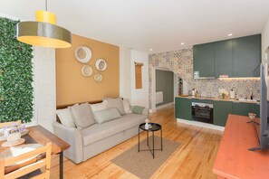 Ein modernes Wohnzimmer mit einer Couch, einem Esstisch und einer Küche mit grünen Schränken und einer gemusterten Spritzschutzleiste.