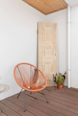 Eine Holztür, ein Korbstuhl und ein Blumentopf auf einer Holzterrasse.