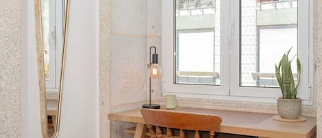 Ein Eckzimmer mit Schreibtisch aus Holz, einem Stuhl, einem Spiegel, einem Fenster und einer Pflanze.