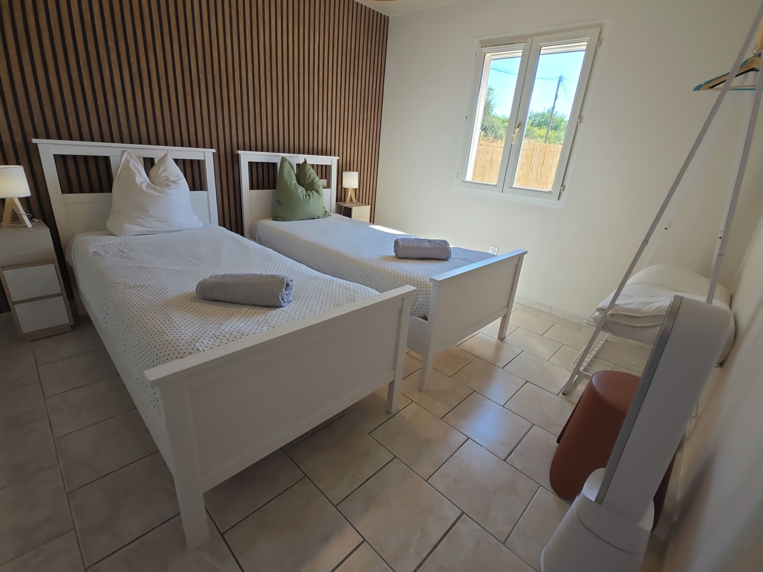 Une chambre avec deux lits, une table de chevet, une commode, une fenêtre et une chaise.