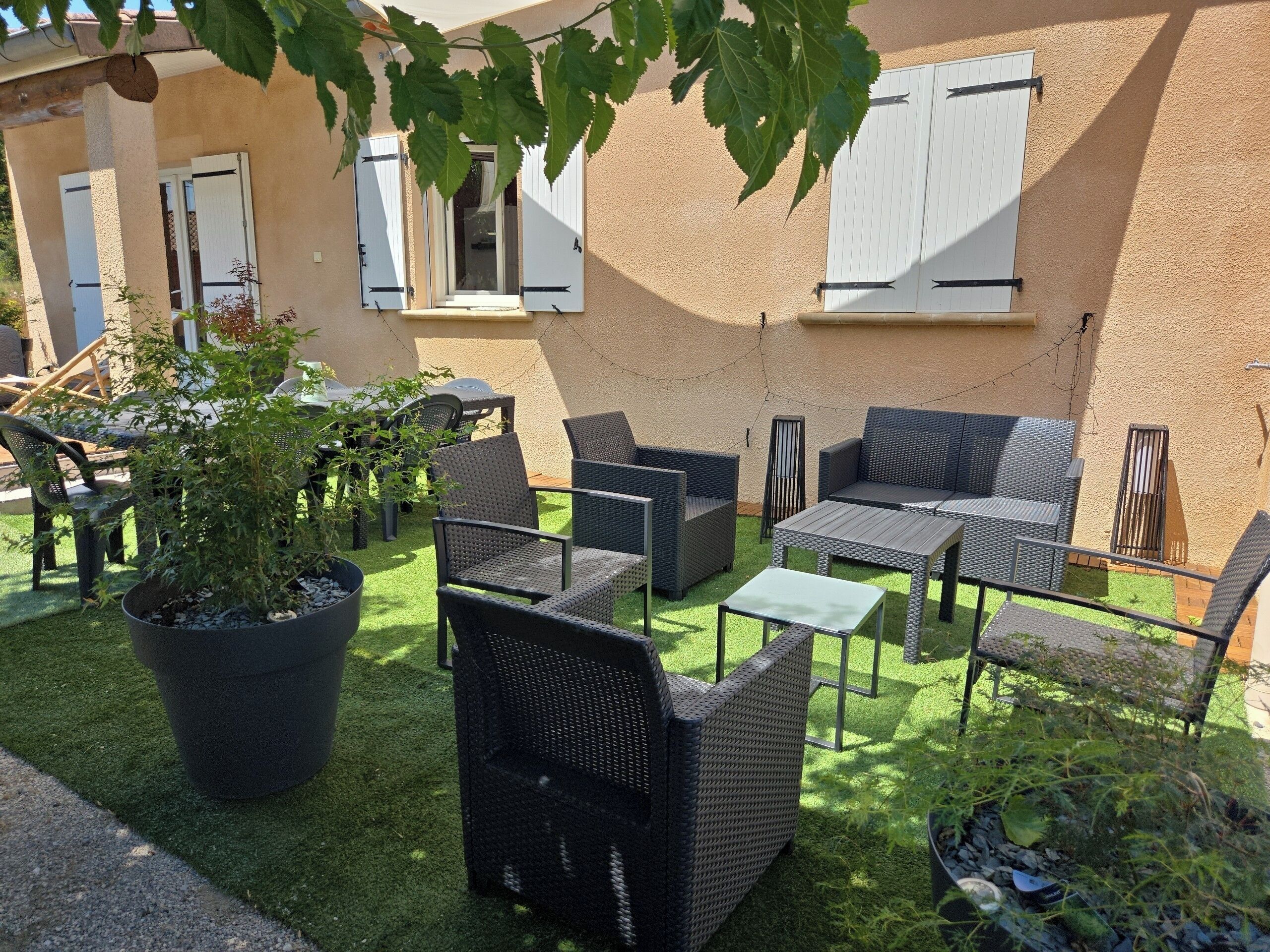 Une terrasse extérieure aménagée avec des meubles en osier, un barbecue et des plantes en pot.