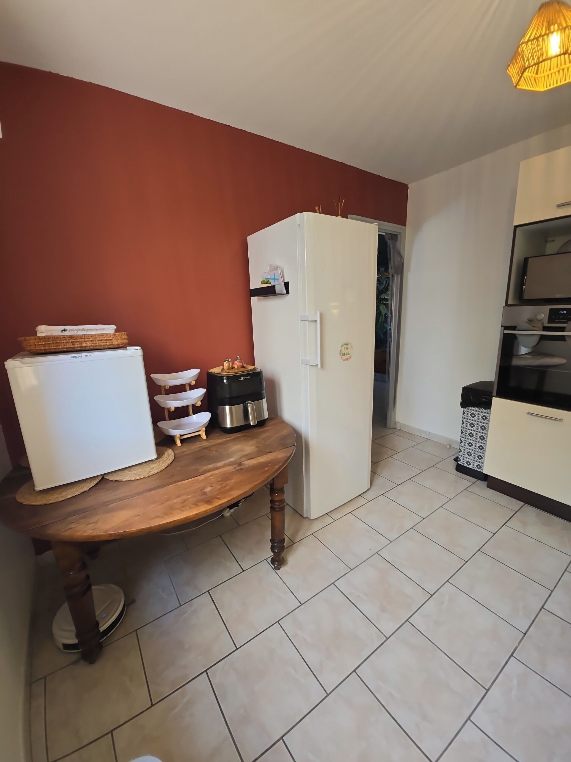 Una cucina compatta con un frigorifero bianco, un tavolo in legno e un pavimento piastrellato.