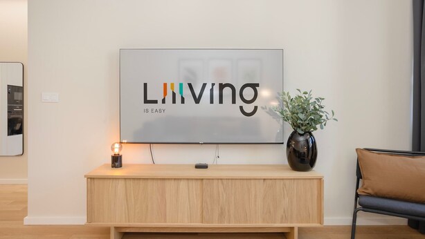 A modern living room with a flat-screen TV mounted on a wall, a wooden console table, a potted plant, and a sofa. - Liiiving in Matosinhos - Mercatus Apartment C (Matosinhos)