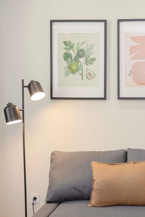 A framed botanical illustration, a modern floor lamp, and a grey sofa with a brown pillow. - Liiiving in Matosinhos - Mercatus Apartment C (Matosinhos)