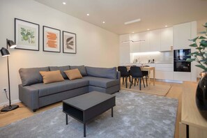 Una sala de estar moderna con un sofá seccional gris, una mesa de centro negra y un comedor con una mesa pequeña y sillas.