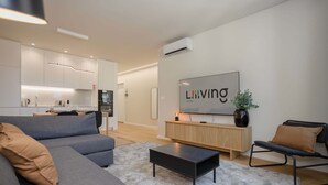 A modern living room with a grey sofa, a black coffee table, a wooden sideboard, and a TV mounted on the wall. - Liiiving in Matosinhos - Mercatus Apartment C (Matosinhos)
