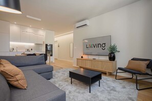 A modern living room with a grey sofa, a black coffee table, a wooden sideboard, and a TV mounted on the wall. - Liiiving in Matosinhos - Mercatus Apartment C (Matosinhos)