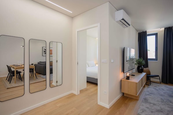 Habitación de hotel moderna con zona de comedor, cama, televisor y mesita de noche con una planta.