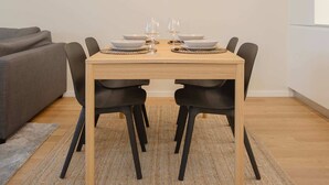 A dining area with a wooden table, black chairs, and a gray sofa in the background. - Liiiving in Matosinhos - Mercatus Apartment C (Matosinhos)