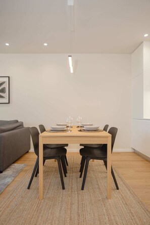 A dining area with a wooden table, black chairs, and a gray sofa in the background. - Liiiving in Matosinhos - Mercatus Apartment C (Matosinhos)