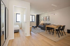 Una sala moderna con sofá, mesa de comedor, sillas, una pequeña mesa auxiliar y una cama en la habitación contigua.