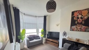 A living room with a grey sofa, a flat-screen TV, a potted plant, and a painting on the wall. - 1 Bedroom Beach View Apartment Sleeps 4 (Rhyl)