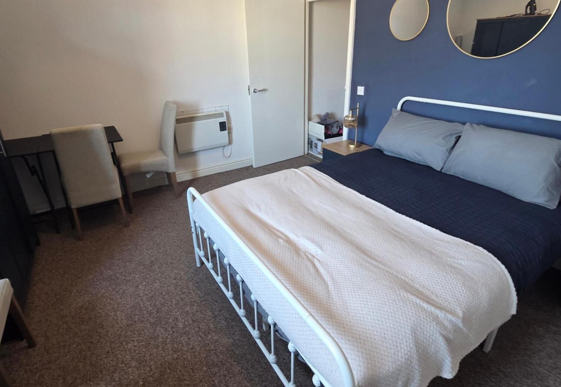 Habitación de hotel con cama, una silla, un escritorio, una mesita de noche, un espejo y un calentador fijado a la pared.