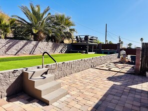 A paved pathway leading to a building with a stone wall and palm trees in the background. - The Rusty Road Runner-Spacious 4-bedroom house in superb Lake Havasu City (Lake Havasu City)