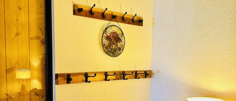 A room with a wooden door, a wall-mounted coat rack, a decorative plate, a lamp, and a small cabinet with drawers.
