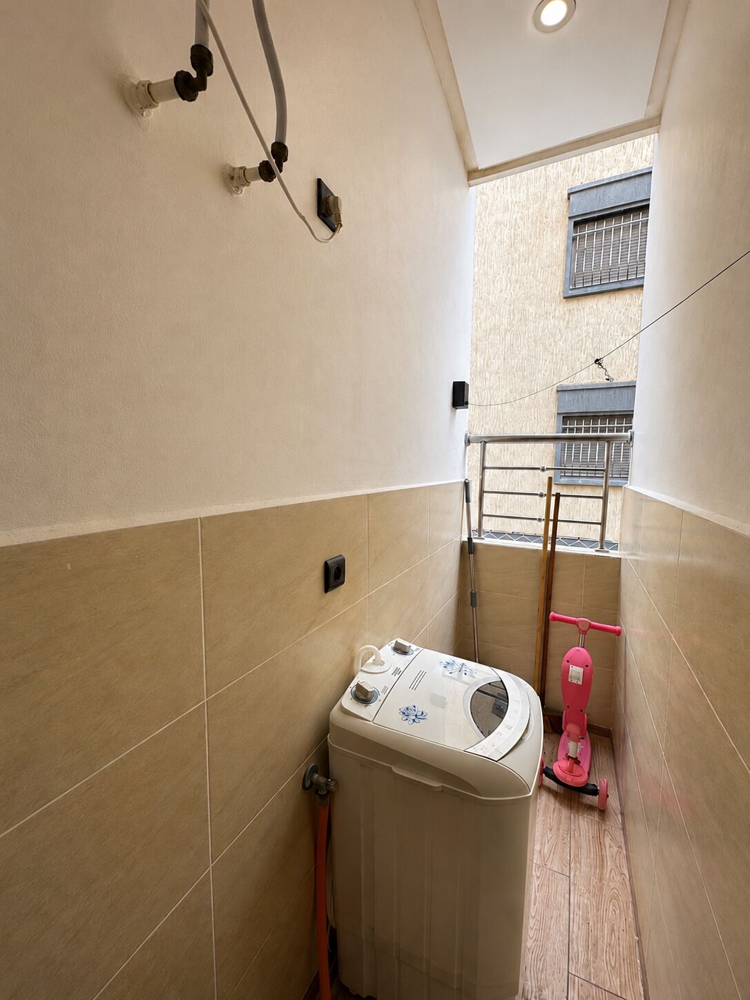A laundry room with a washing machine, a mop, and a window with a view of the outside.