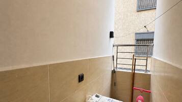 A laundry room with a washing machine, a mop, and a window with a view of the outside.